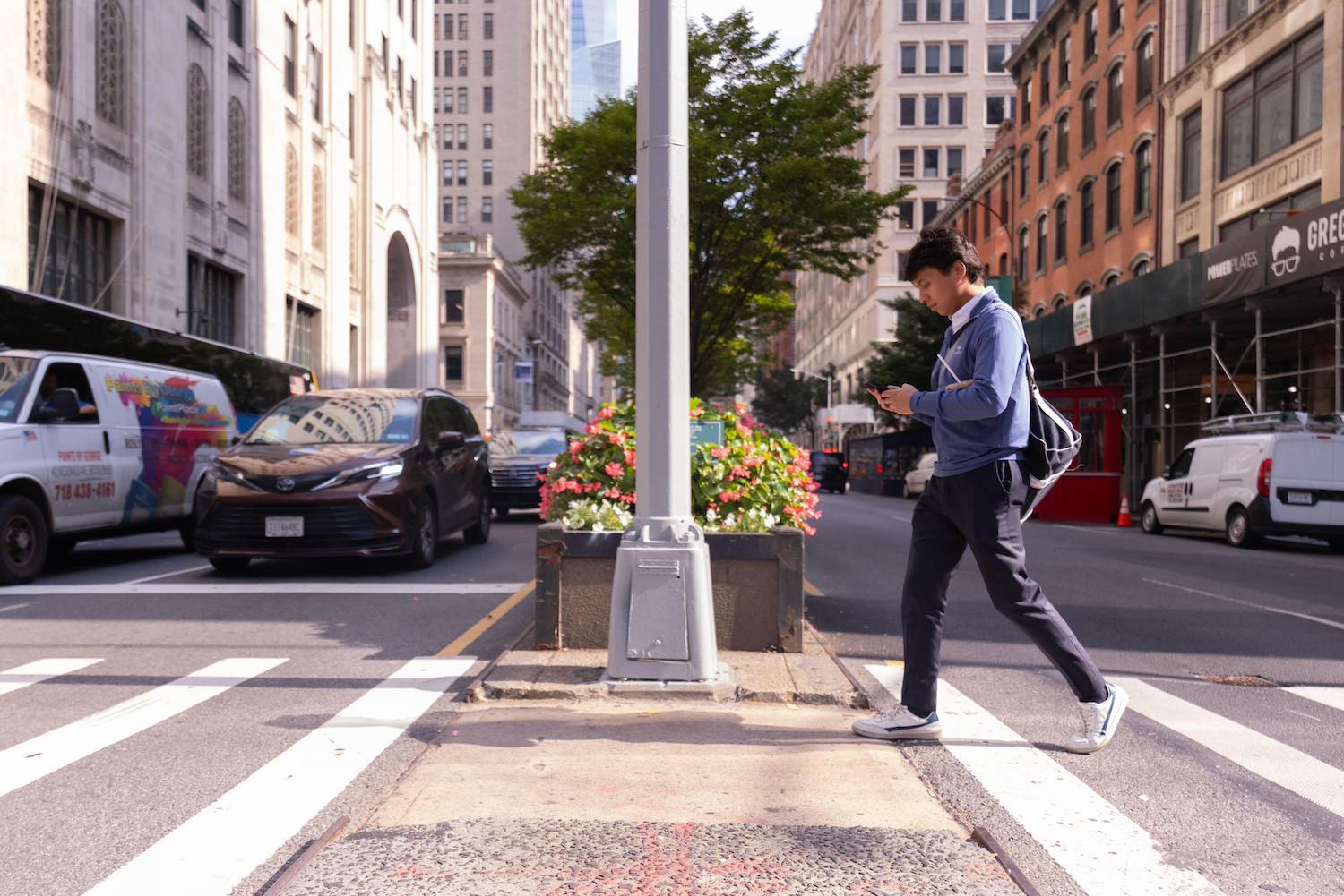 Candid photo of Kevin Chong crossing the street looking at his phone. 