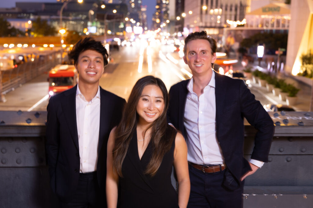 All three alumni smiling for a picture with New York City behind them.