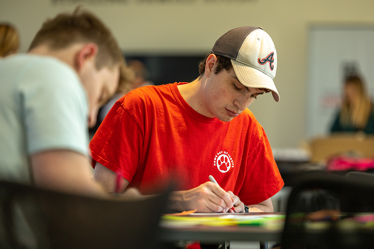 A male student in a Braves hat writes a note to be packed into B.A.G. backpack