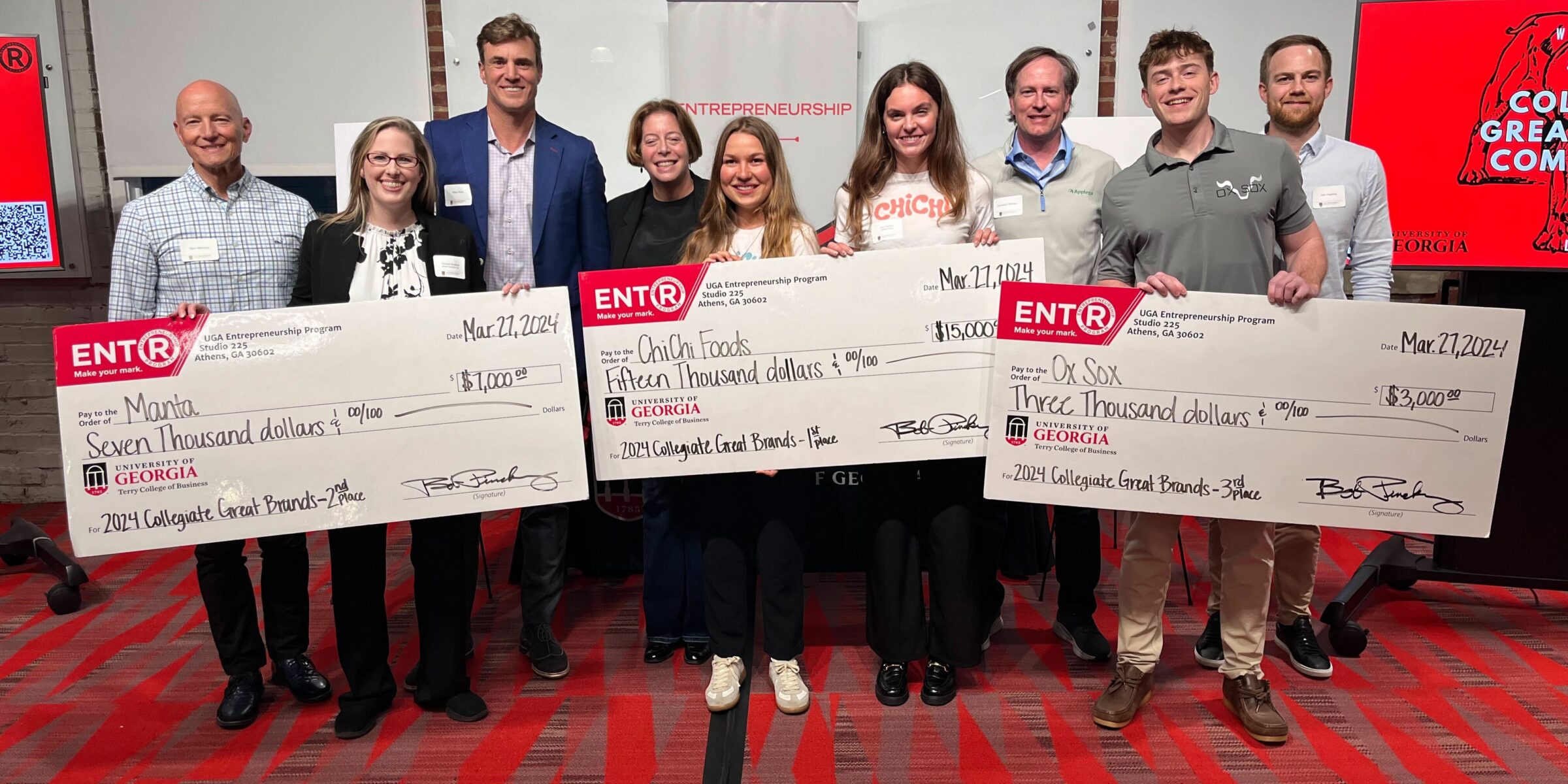 Winners of the 2024 Collegiate Great Brands pitch competition stand with their novelty prize checks with the contest's four judges behind them at Studio 225.