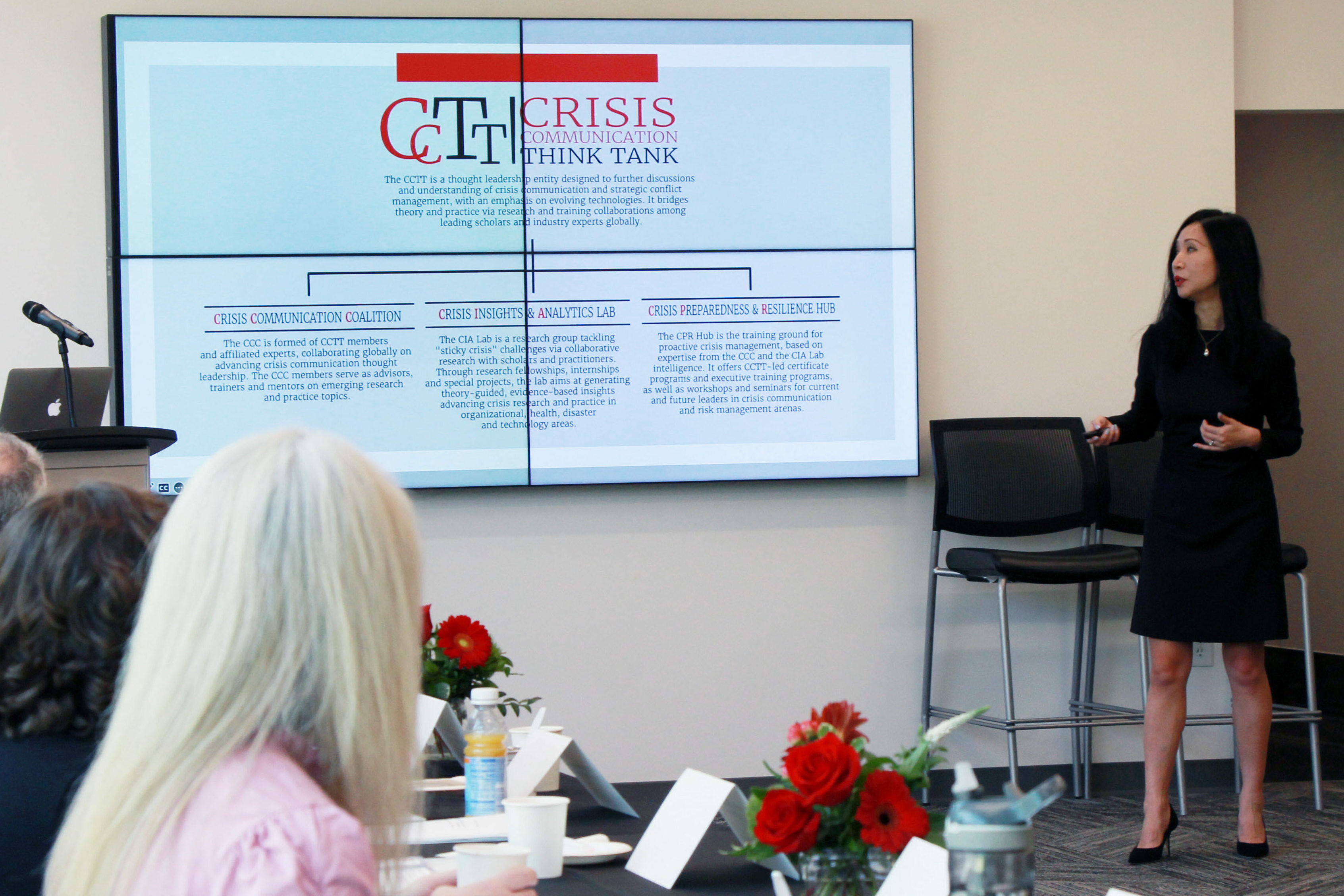 A woman presents to a group of people in front of a TV screen.