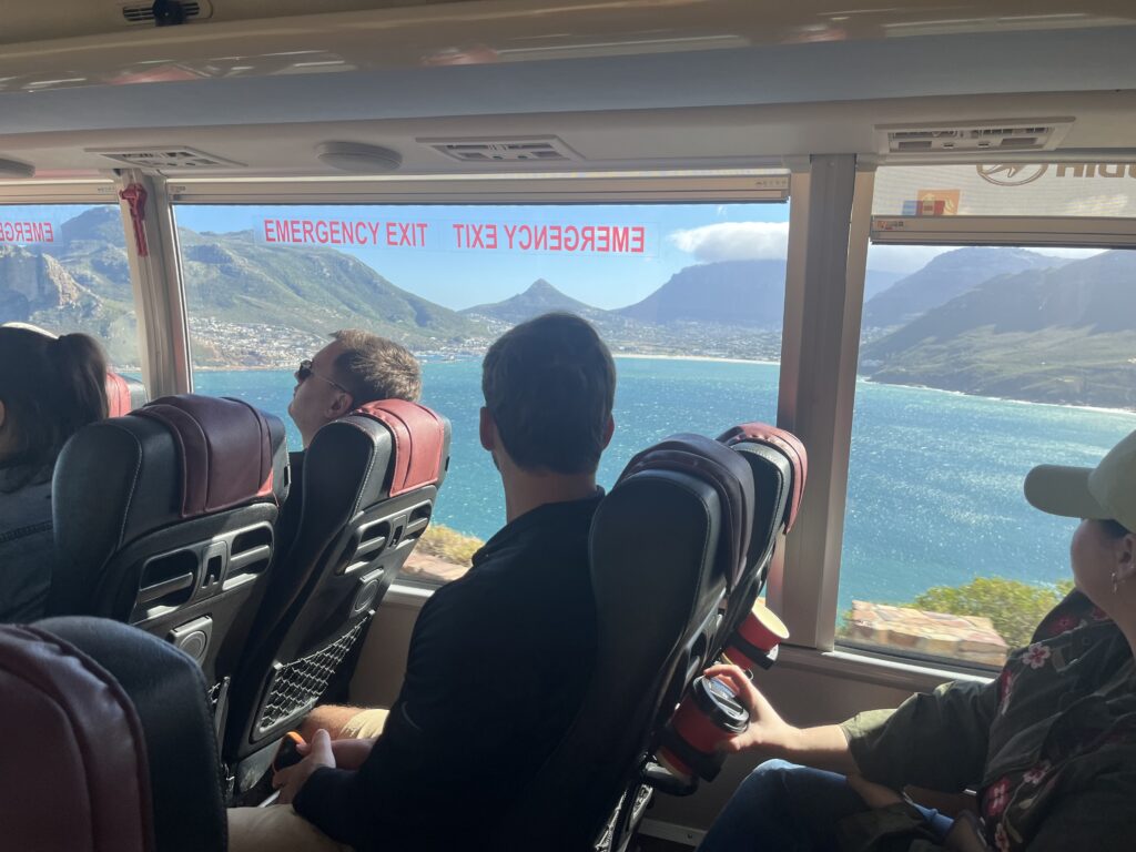 Terry College MBA students look out the window of a bus to look at the ocean with a city and mountains in the distance.